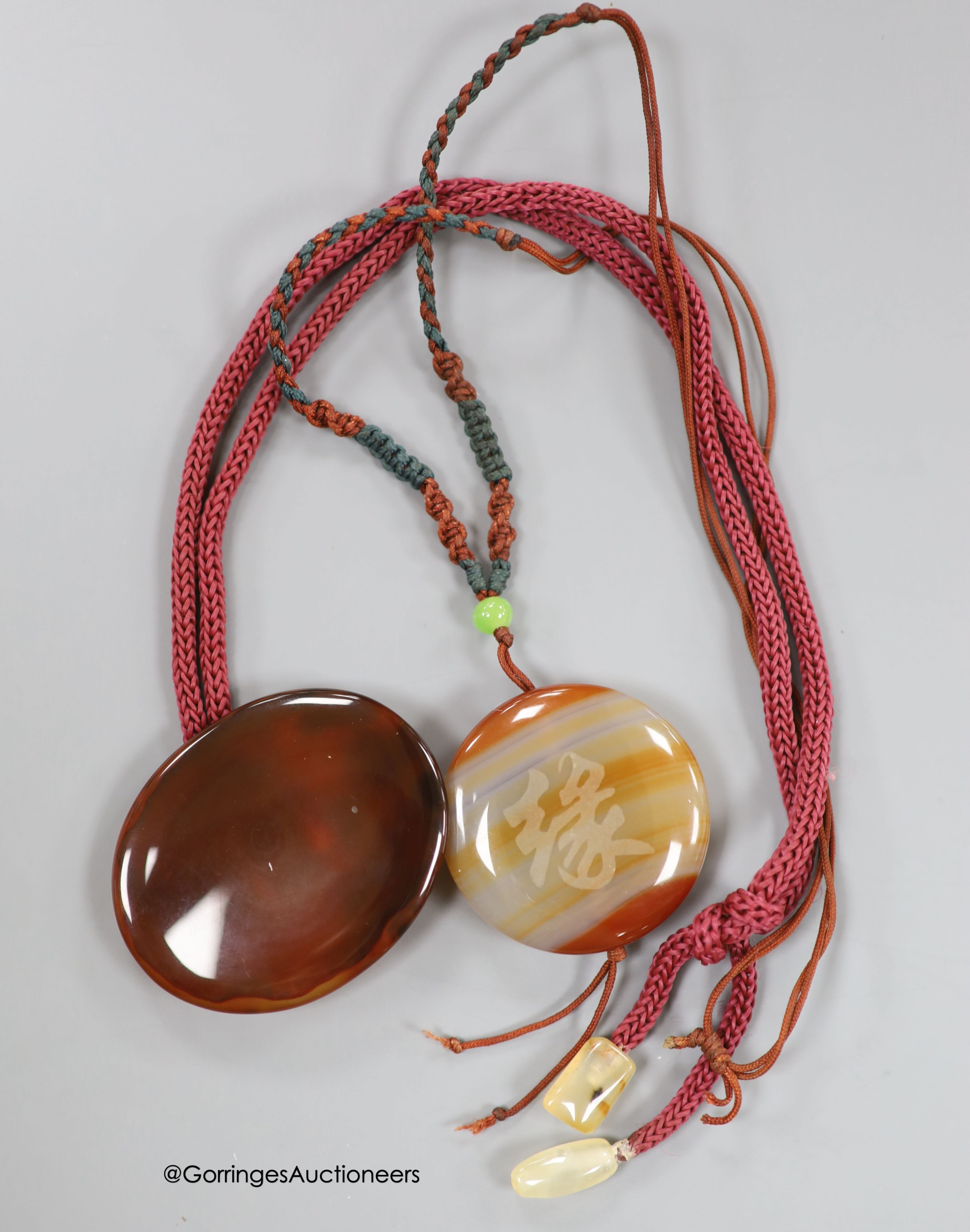 Two agate pendants, on fabric cords, largest pendant 57mm.